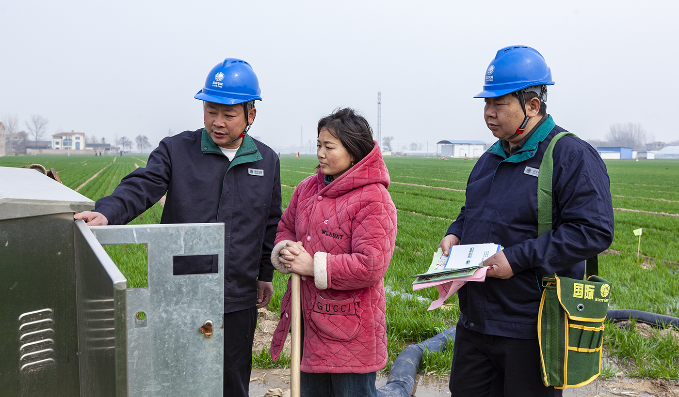 麦田里，绿油油的麦苗正畅饮着返青水，而那一支支穿梭其间的电力服务队，正默默守护着这一季的丰收希望。图为，2026年3月16日上午，国网滑县供电公司电力服务队队员康玉川、赵强在八里营镇东风村麦田，检查春灌用电设备并提醒村民安全用电。（王亚方 摄）